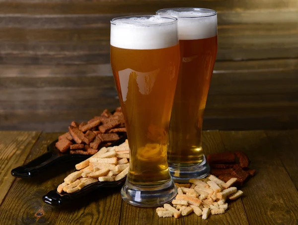 Vasos de cerveza con merienda en la mesa sobre fondo de madera —  Fotos de Stock