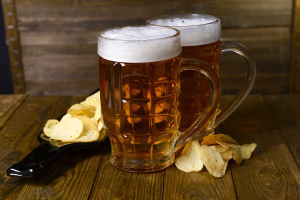 Copos de cerveja com lanche na mesa em fundo de madeira — Fotografia de Stock