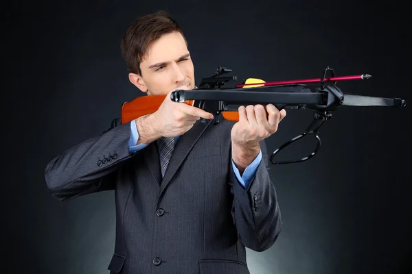 Young businessman with crossbow, on dark background — Stock Photo, Image