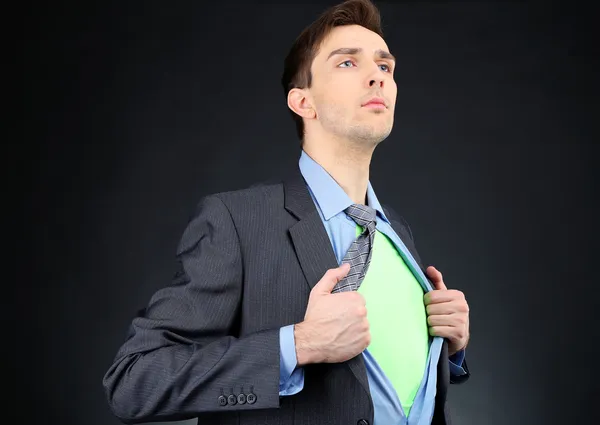 Joven hombre de negocios desgarrando su camisa revelando traje de superhéroe, sobre fondo oscuro —  Fotos de Stock