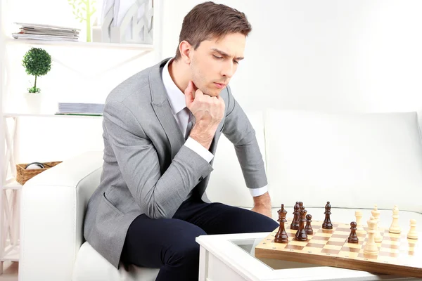 Elegant young businessman sitting on sofa and playing chess, at home — Stock Photo, Image