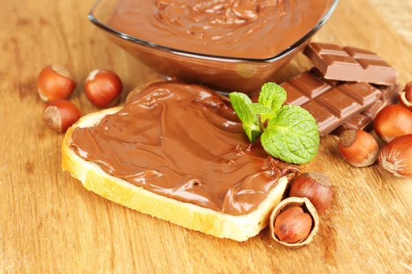 Pão com avelã de chocolate doce espalhado no fundo de madeira — Fotografia de Stock