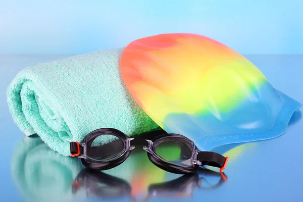 Conjunto para piscina: touca de natação, óculos e toalha sobre fundo azul — Fotografia de Stock