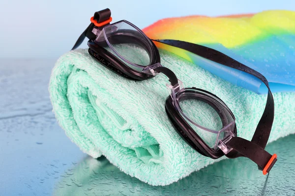 Комплект для бассейна: плавательная шапочка, очки и полотенце на синем фоне — стоковое фото