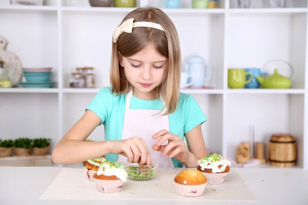 Little girl decorating cupcakes in kitchen at home Stock Photo