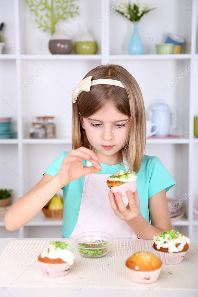 Little girl decorating cupcakes in kitchen at home — Stock Photo