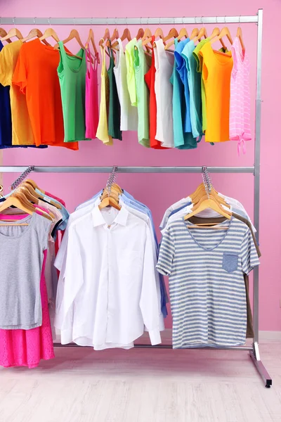 Different clothes on hangers, on pink background — Stock Photo, Image