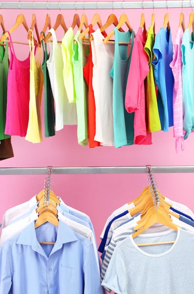 Different clothes on hangers, on pink background — Stock Photo, Image