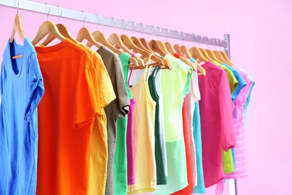 Different clothes on hangers, on pink background — Stock Photo, Image