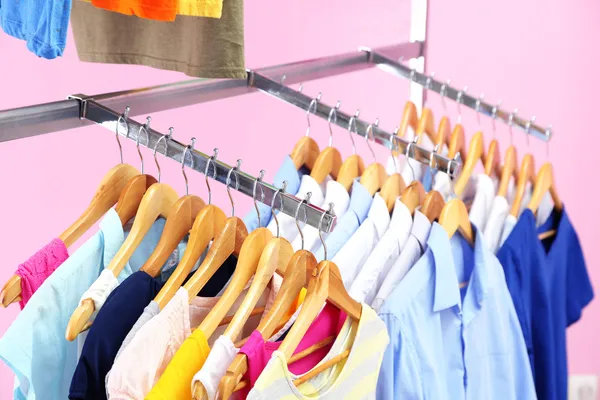 Διαφορετικά ρούχα σε κρεμάστρες, σε ροζ φόντο — Φωτογραφία Αρχείου