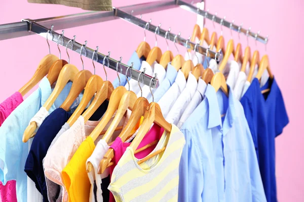 Verschillende kleding op hangers, op roze achtergrond — Stockfoto