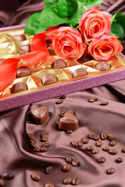 Läckra chokladpraliner i låda med blommor på brun bakgrund — Stockfoto