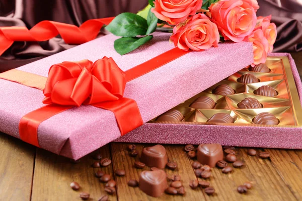 Delicious chocolates in box with flowers on table on brown background — Stock Photo, Image