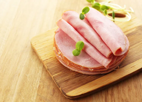 Tasty ham with sunflower sprouts on wooden background — Stock Photo, Image