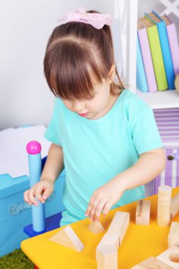küçük kız odasındaki masada oturan inşaat blokları ile oynuyor.