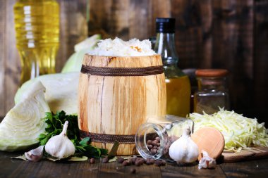 Composition with fresh and marinated cabbage (sauerkraut) in wooden barrel, on wooden table background clipart