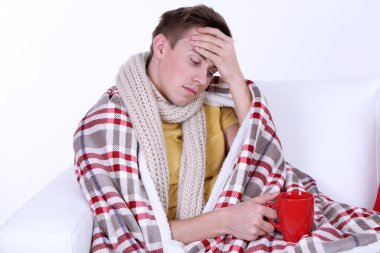 Guy wrapped in plaid lies on sofa on white background clipart