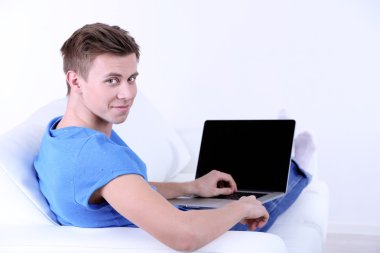 beyaz zemin üzerinde laptop ile kanepede oturan adamı
