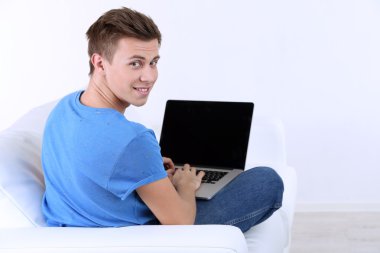 beyaz zemin üzerinde laptop ile kanepede oturan adamı