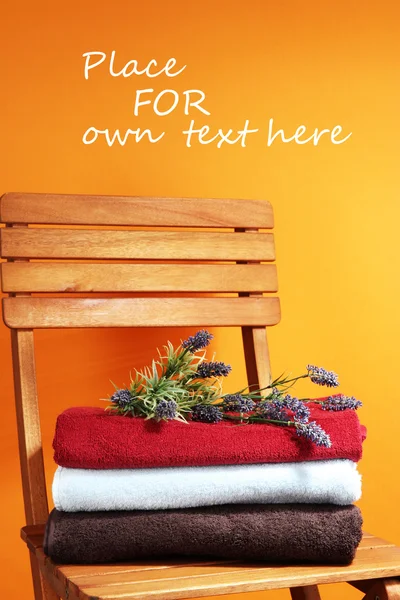 Towels and flowers on wooden chair on orange background — Stok fotoğraf