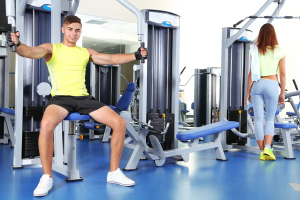 Chico y chica involucrados en simulador en el gimnasio —  Fotos de Stock