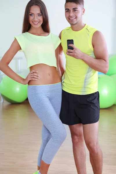 Guy and girl photographing in mirror at phone in fitness room