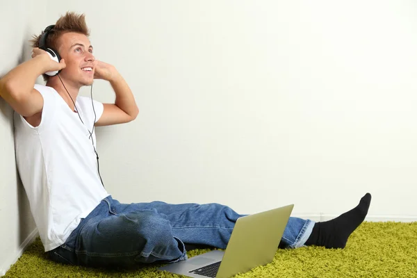 Jonge man ontspannen op tapijt en luisteren naar muziek, op grijze muur achtergrond — Stockfoto