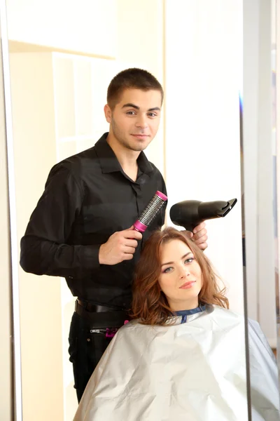 Молодой парикмахер делает прическу девушке в салоне красоты — стоковое фото