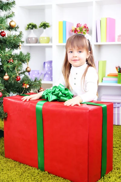 Little girl with big present box near Christmas tree in room — Stock Photo, Image