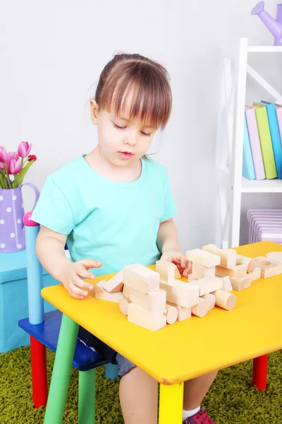 Little girl plays with construction blocks sitting at table in room — Stock Photo, Image