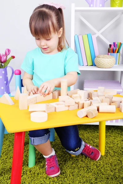 Little girl plays with construction blocks sitting at table in room — Stock Photo, Image