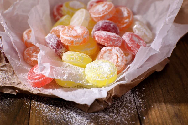 Sweet multicolor candies on paper, on wooden background — Stock Photo, Image