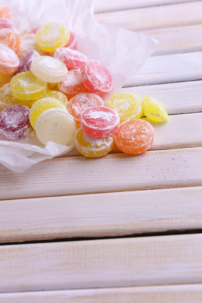 Dulces caramelos multicolores sobre papel, sobre fondo de madera de color — Foto de Stock
