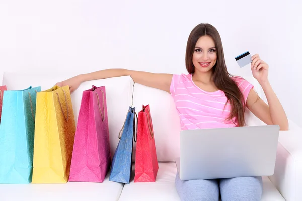 Piękna młoda kobieta trzymając laptop z torby na zakupy na kanapie na białym tle — Zdjęcie stockowe