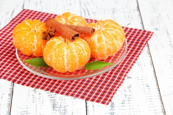 Ripe sweet tangerines with spices on color plate, on napkin, on wooden background — Stock Photo, Image