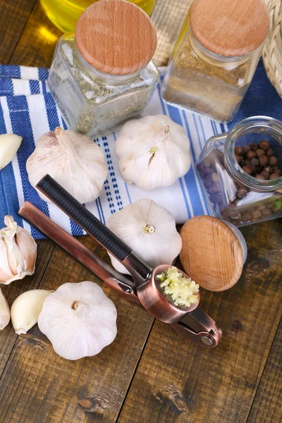 Samenstelling met knoflook press, verse knoflook en glazen potten met specerijen op houten achtergrond — Stockfoto