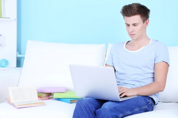 Man zittend op de Bank met laptop op blauwe achtergrond — Stockfoto