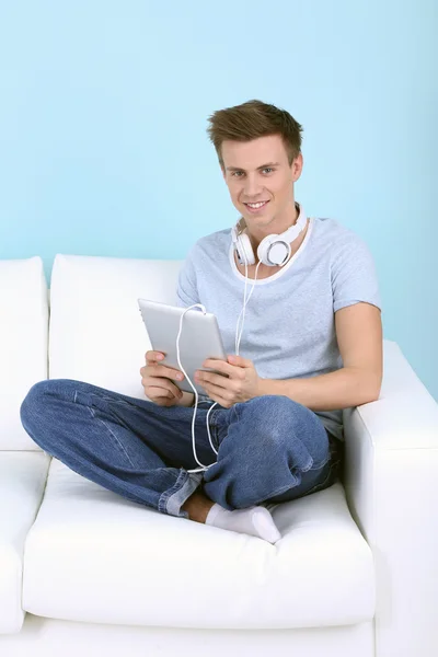 Guy sitting on sofa and listening to music on blue background — Stock Photo, Image