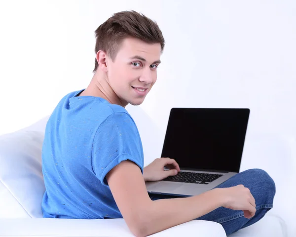 Cara sentado no sofá com laptop no fundo branco — Fotografia de Stock