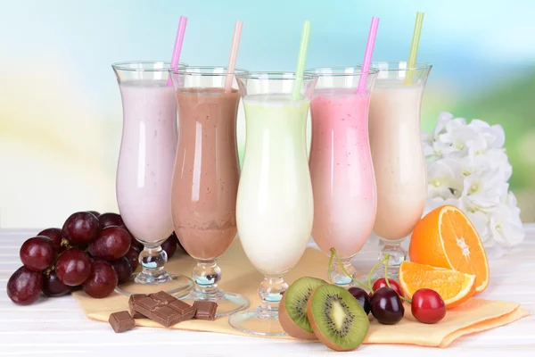 Milk shakes with fruits on table on light blue background — Stock Photo, Image