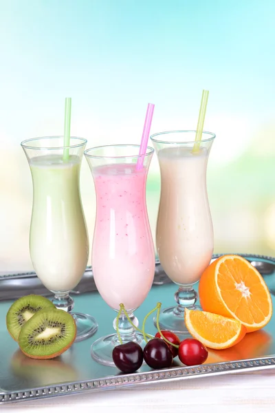 Milk shakes with fruits on table on light blue background — Stock Photo, Image