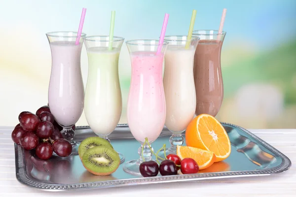 Milk shakes with fruits on table on light blue background — Stock Photo, Image