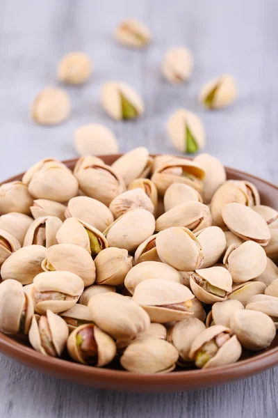 Pistachio nuts on plate on wooden background — Stock Photo, Image