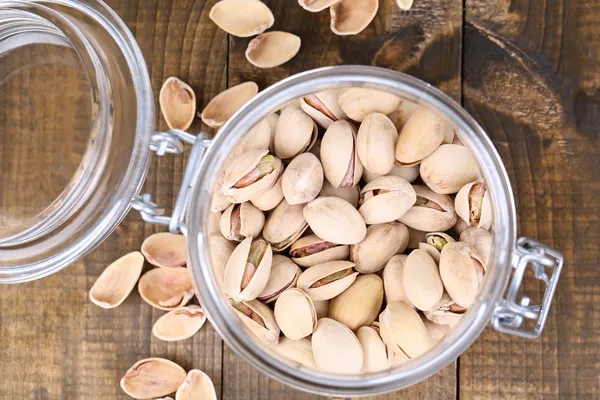 Pistachio nuts in glass jar on wooden background — Stock Photo, Image