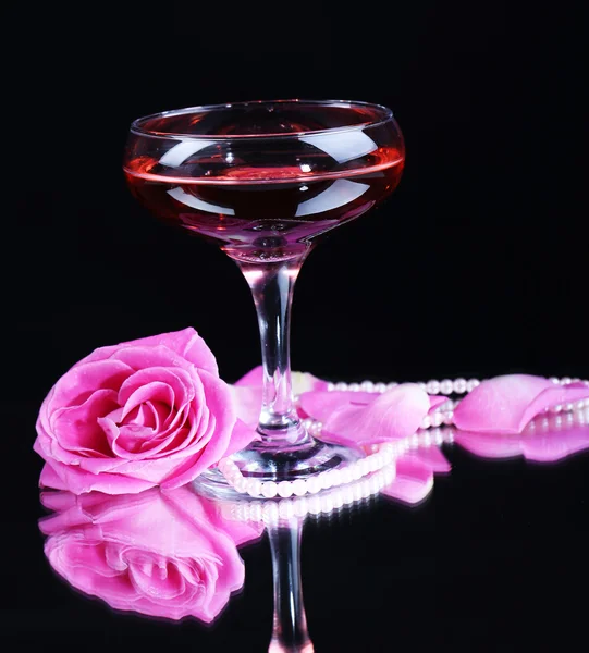 Komposition mit rosa Sekt im Glas und Rose isoliert auf schwarz — Stockfoto