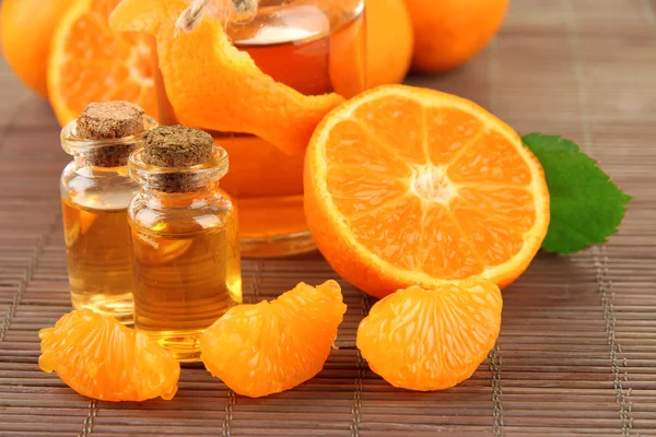 Tangerine essential oil and tangerines on grey bamboo mat — Stock Photo, Image