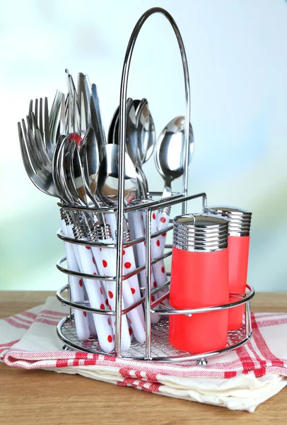 Kitchen cutlery in metal stand on wooden table on bright background — Stock Photo, Image