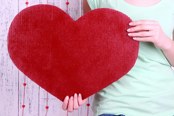 Vrouwelijke houden grote rood hart op houten achtergrond — Stockfoto