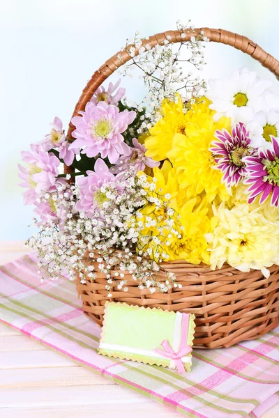 Beautiful chrysanthemum flowers in wicker basket on table on light background — Stock Photo, Image