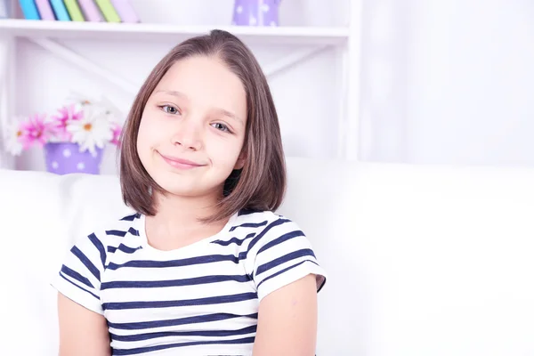 Beautiful little girl sitting on sofa, on home interior background — Stock Photo, Image